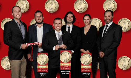 winner-2-years-in-a-row Six people in formal attire smile and pose in front of a red backdrop with gold Local Business Awards logos. Three people hold trophies and award signs for Business of the Year and Outstanding Service & Trade.
