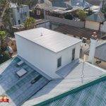 Aerial view of a white, modern rooftop extension added to a house with a metal roof, surrounded by neighboring homes and trees in a suburban area. 32 Degrees Building logo is visible in the bottom left corner.