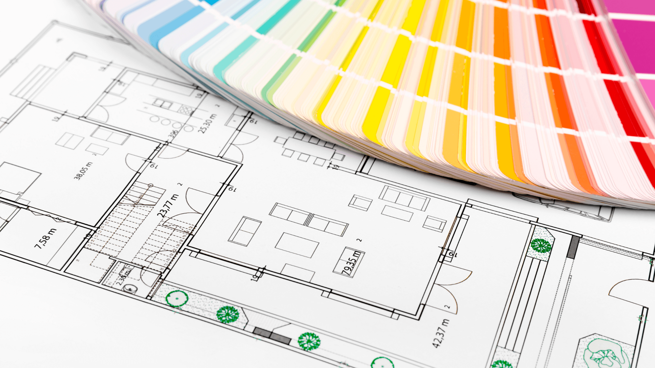 A close-up of a color swatch fan displaying various paint shades, placed on top of a detailed architectural floor plan drawing of a house.