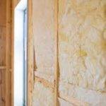 Insulation - Upgrade Internal Walls Close-up of a wall with yellow fiberglass insulation installed between wooden studs, next to a window frame, showing construction or renovation work in progress.