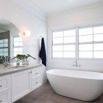 Windows - Upgrade Double Hung Bright, modern bathroom with a freestanding white bathtub near large windows, a double-sink vanity with a mirror, and white cabinetry. A navy towel hangs on the wall next to the tub.